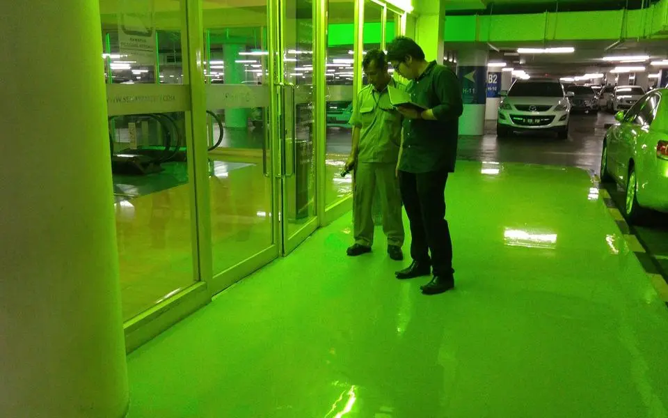 Dua orang memeriksa lantai epoxy hijau di basement parkir Senayan City