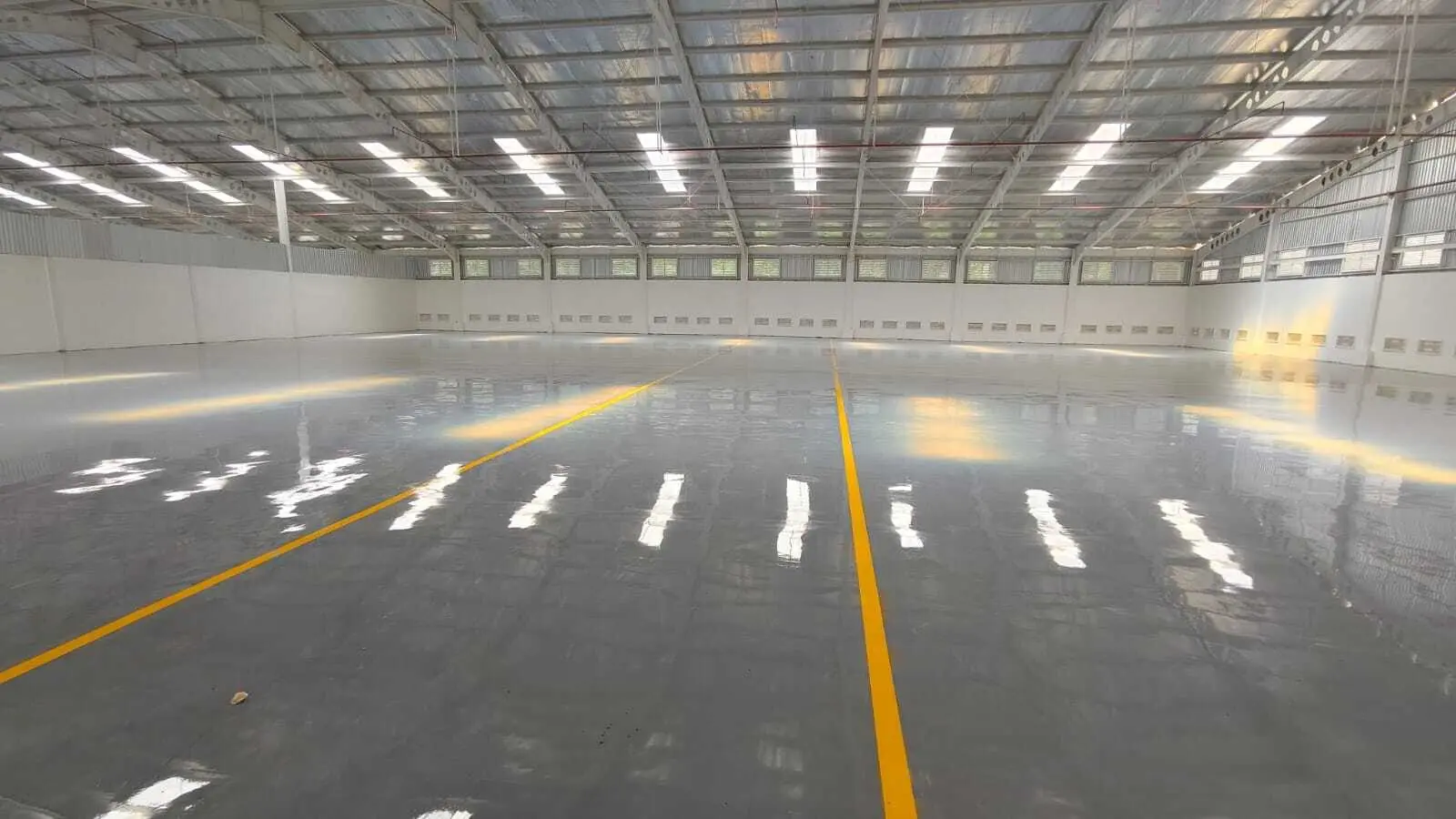 Lantai gudang industri dengan epoxy abu-abu dan marka jalur kuning, bentang luas tanpa sambungan