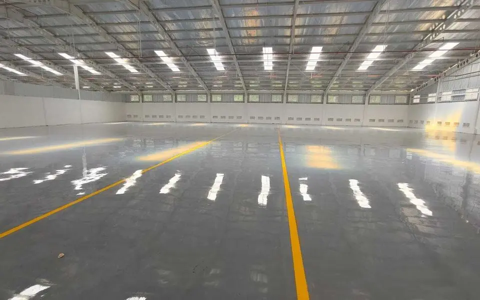 Lantai epoxy abu-abu dengan marka jalur kuning di gudang yang luas