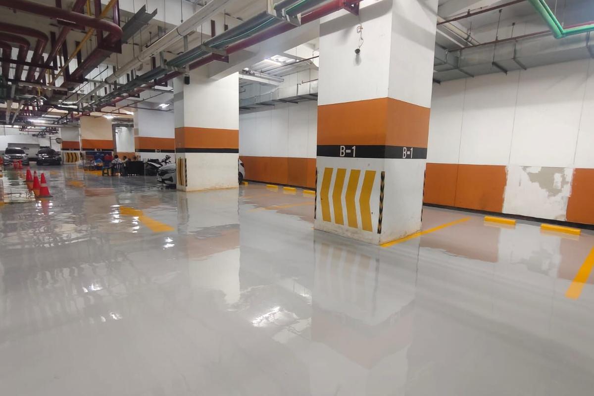 Basement parkir Plaza BPJAMSOSTEK dengan lantai epoxy abu-abu dan kolom bermarka oranye