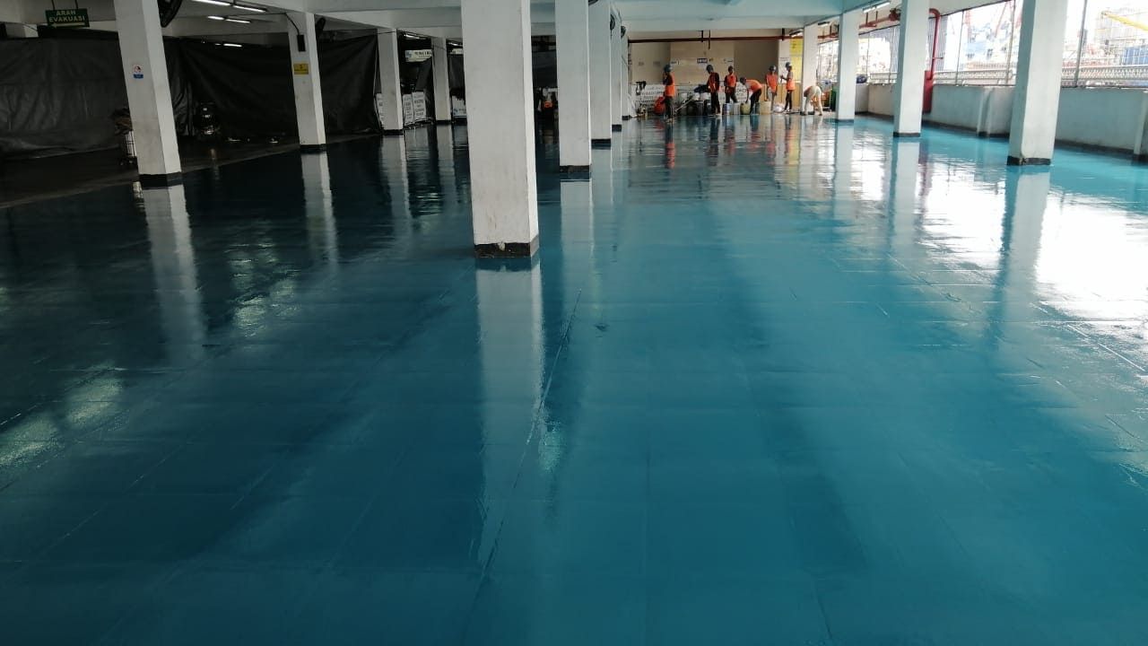 Lantai epoxy biru di gudang Pelindo Tanjung Priok, memanjang di antara deretan kolom (3/6)