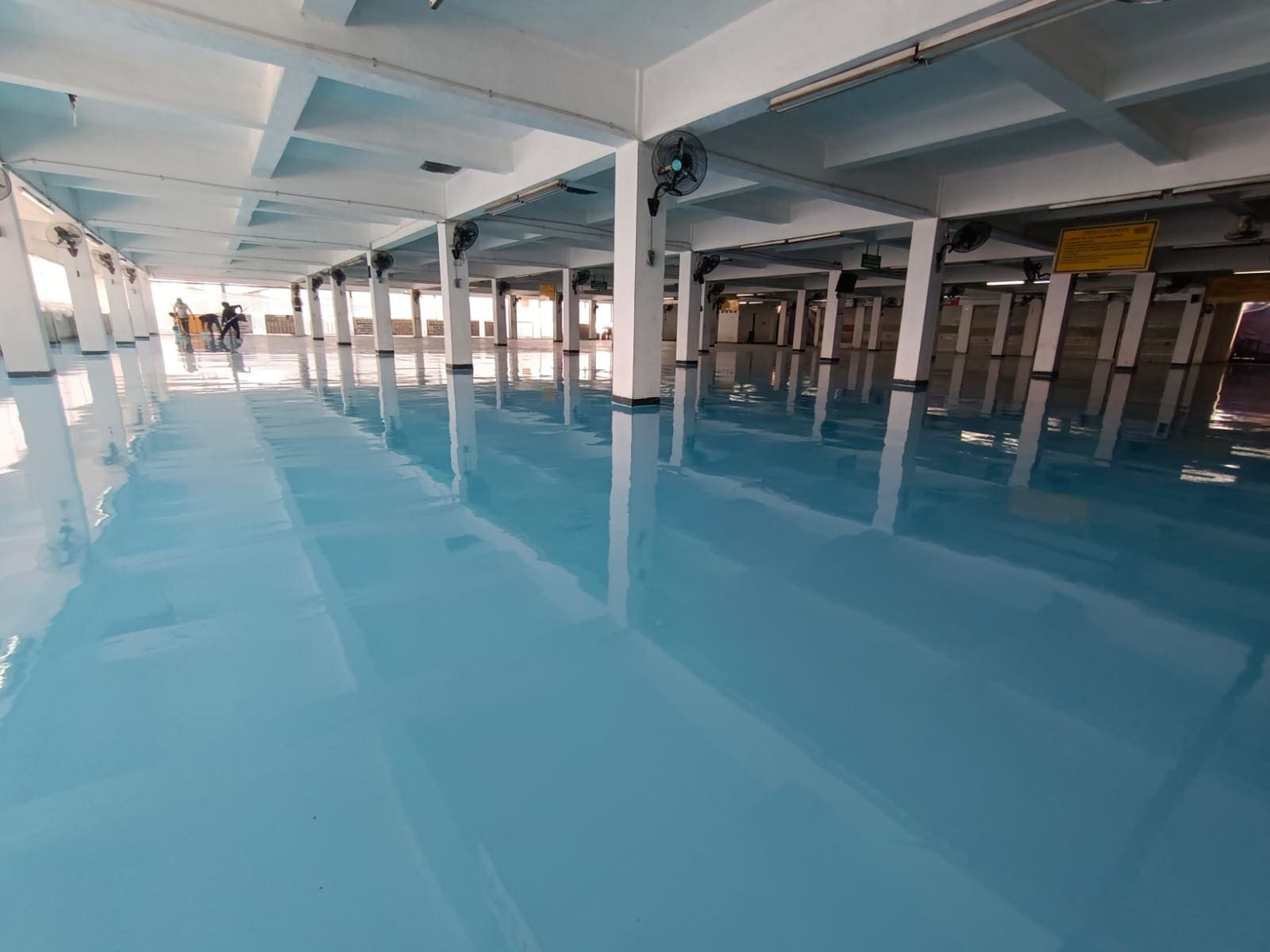 Lantai epoxy biru di gudang Pelindo Tanjung Priok, memanjang di antara deretan kolom (5/6)