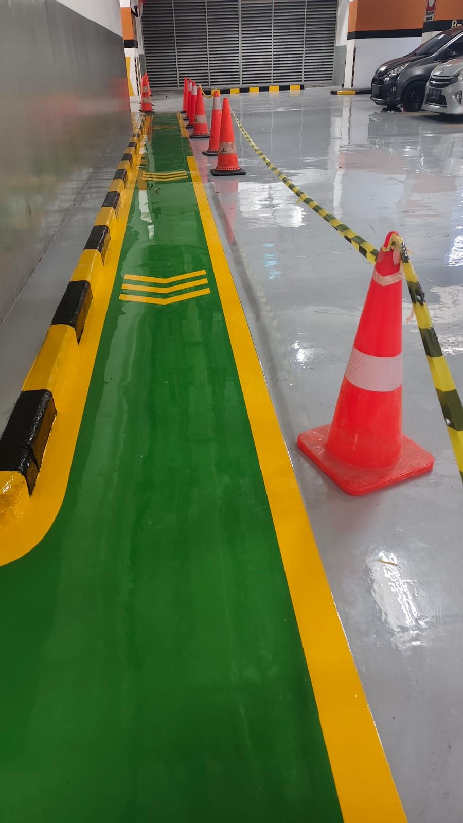 Basement parkir Plaza BPJAMSOSTEK dengan lantai epoxy abu-abu dan kolom bermarka oranye (2/5)