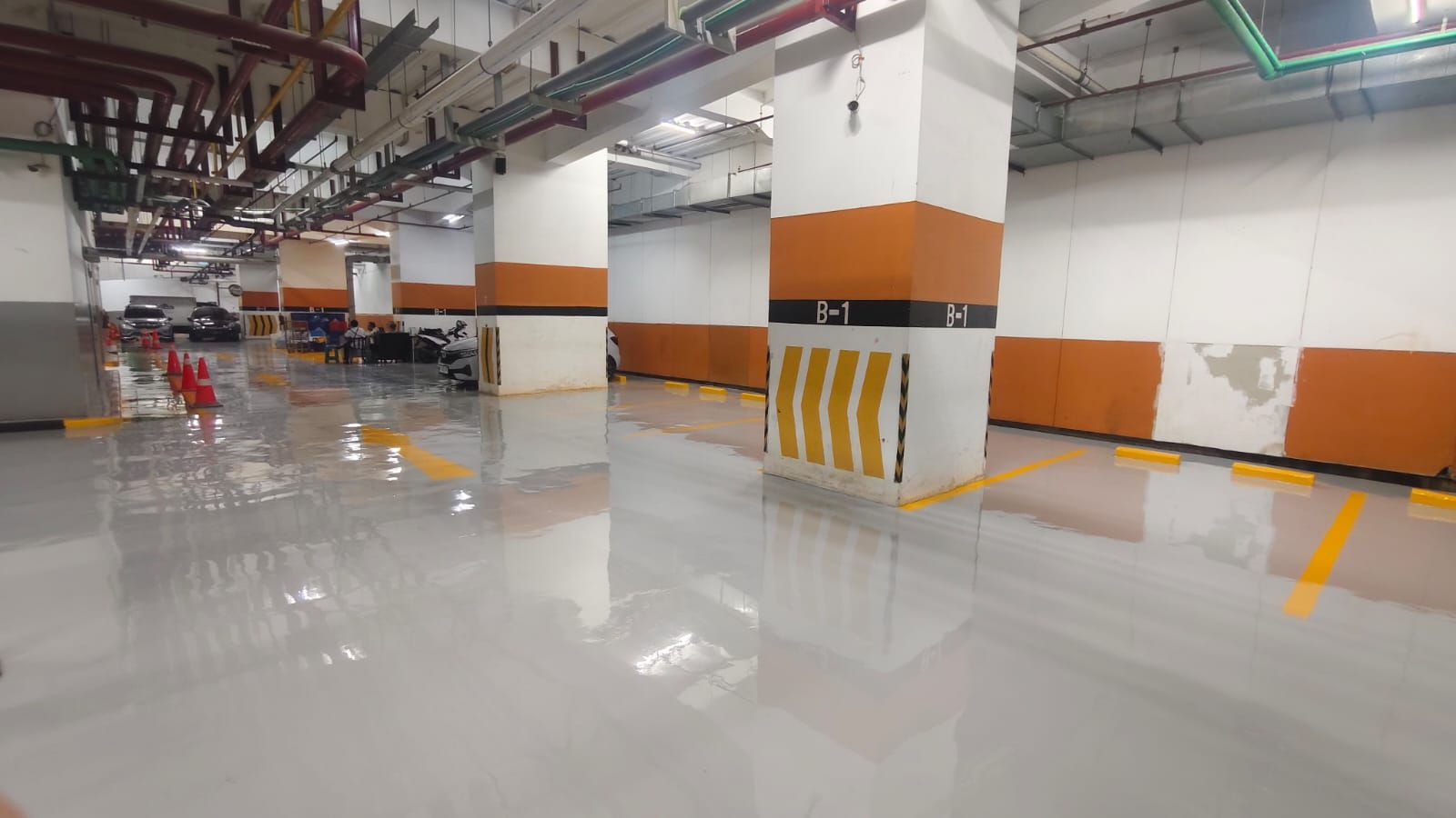 Basement parkir Plaza BPJAMSOSTEK dengan lantai epoxy abu-abu dan kolom bermarka oranye