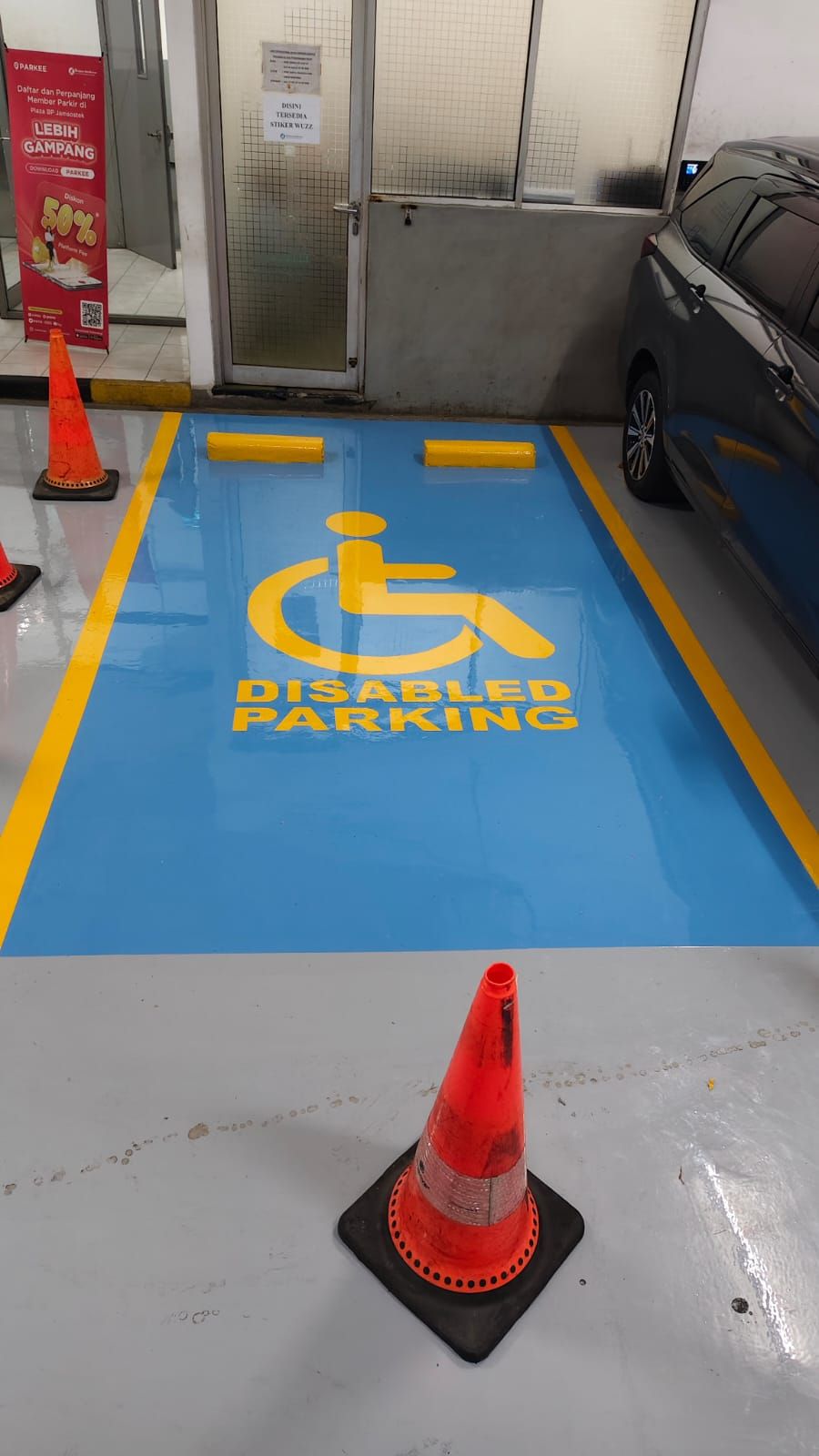 Basement parkir Plaza BPJAMSOSTEK dengan lantai epoxy abu-abu dan kolom bermarka oranye (3/5)