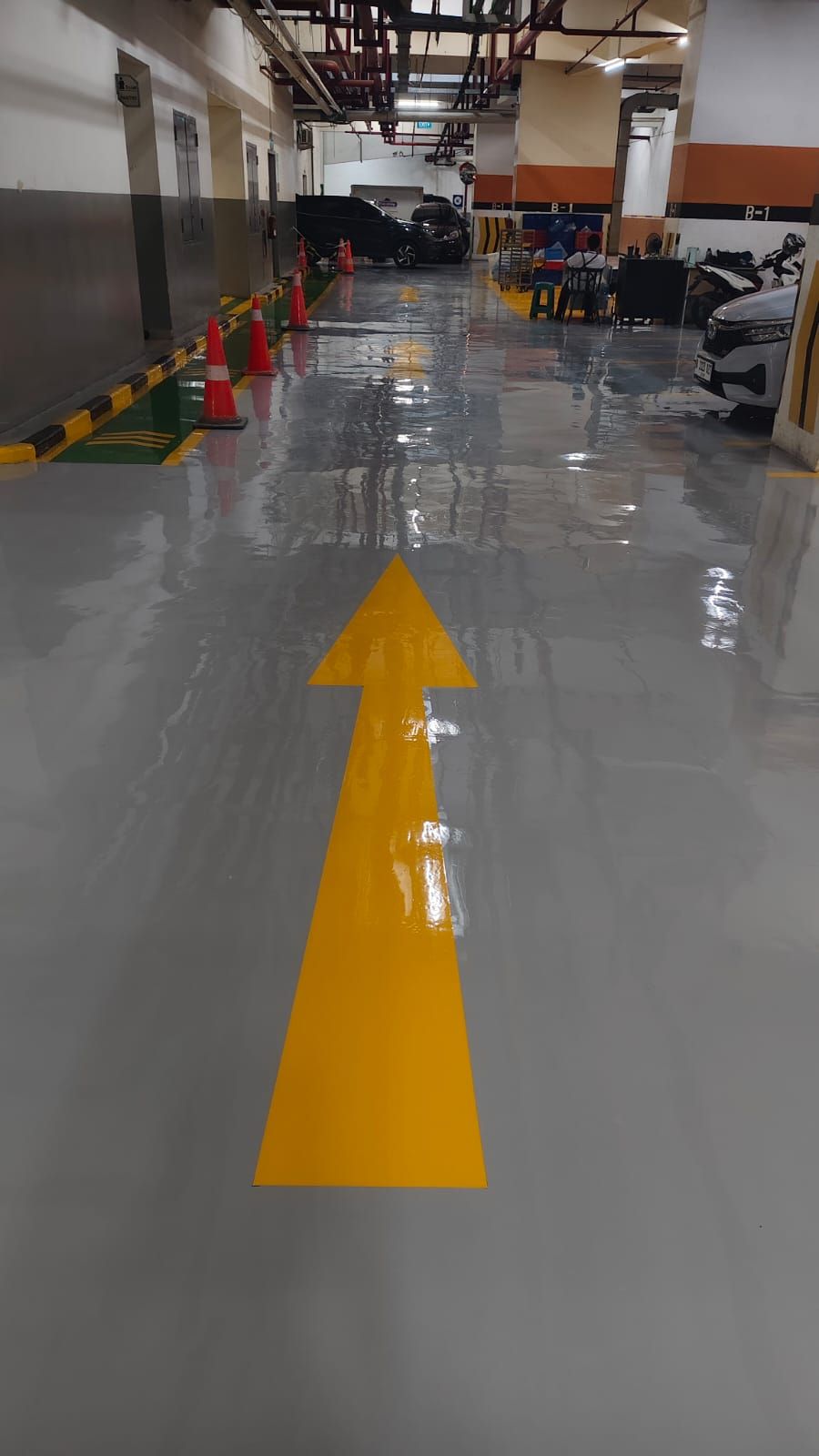 Basement parkir Plaza BPJAMSOSTEK dengan lantai epoxy abu-abu dan kolom bermarka oranye (4/5)