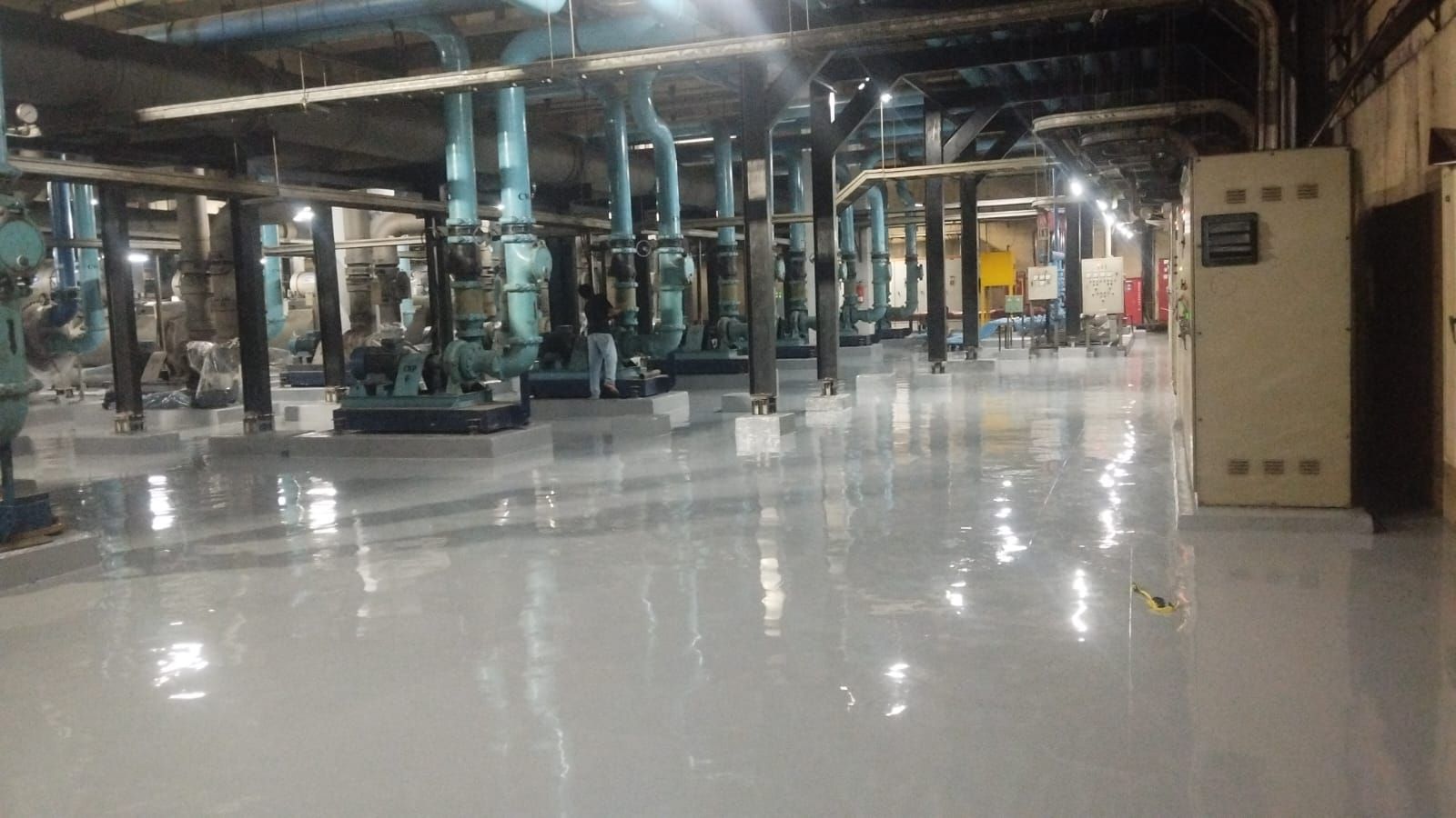 Ruang chiller Plaza Mandiri dengan lantai epoxy abu-abu kebiruan di antara jaringan pipa