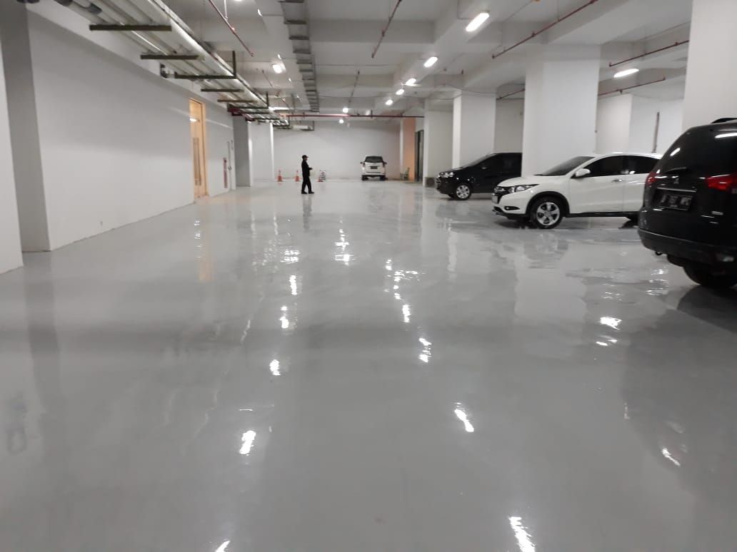 Lantai parkir Sudirman Suites dengan epoxy abu-abu dan mobil terparkir di ujung ruang